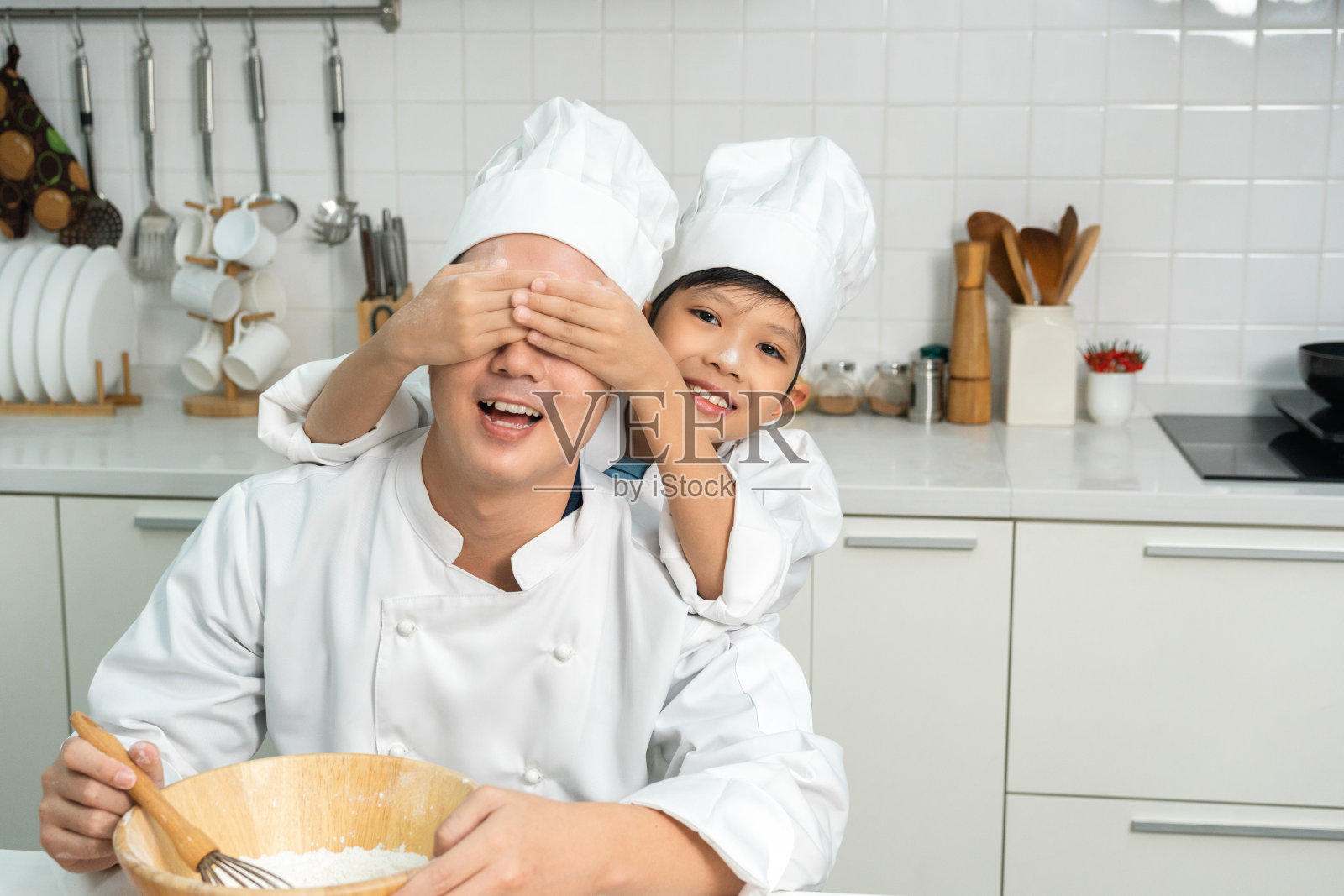 年轻英俊的亚洲男厨师在厨房做早餐。快乐的亚洲人用配料准备食物。厨房里穿制服的厨师。照片摄影图片