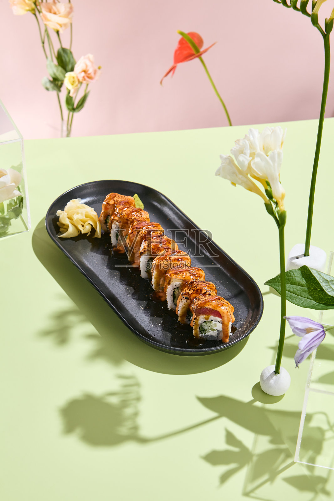 时尚的寿司设置与烤金枪鱼卷,黄瓜和辣酱在极简主义的花卉背景照片摄影图片