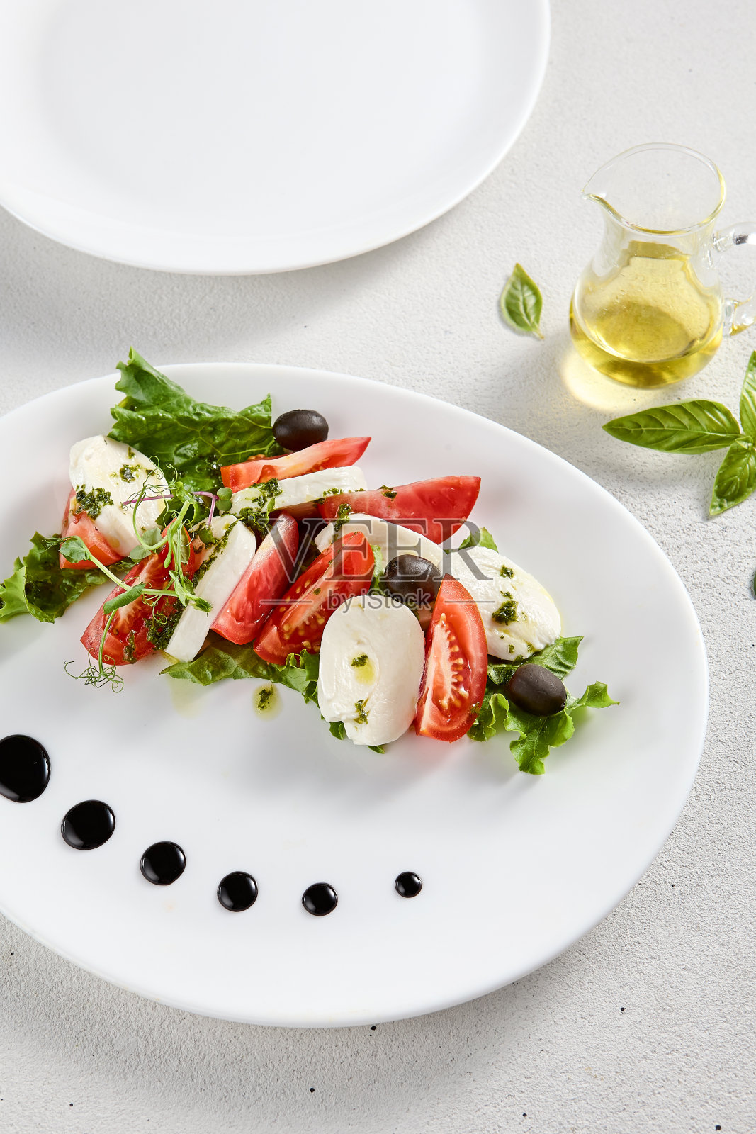 经典的卡普里斯沙拉,配以成熟的西红柿、马苏里拉奶酪和橄榄,配以新鲜的罗勒。适合意大利美食促销和烹饪书籍照片摄影图片