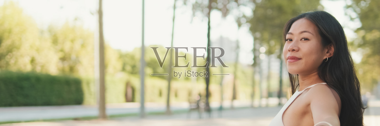 漂亮的黑发女孩,穿着白色上衣和牛仔裤,坐在公园的长椅上,享受着好天气,空闲时间,全景照片摄影图片