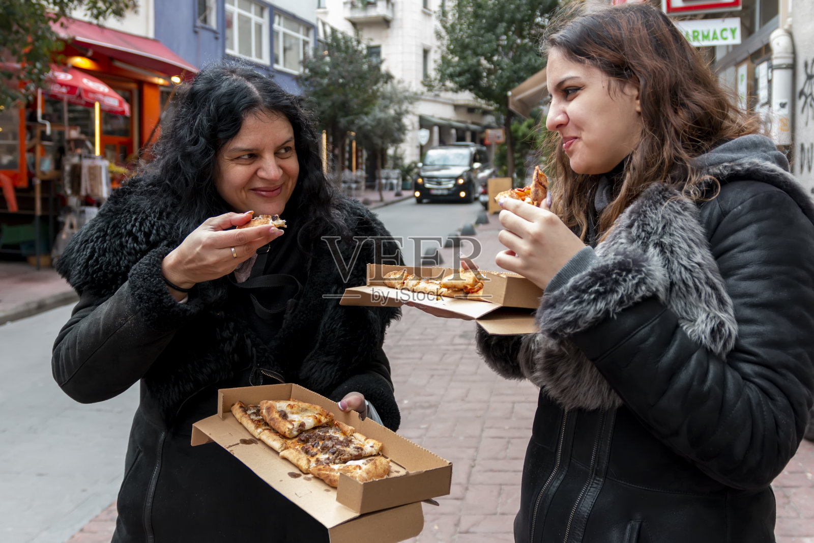 冬天,妈妈和女儿一起在街上吃着盒子里的披萨。照片摄影图片