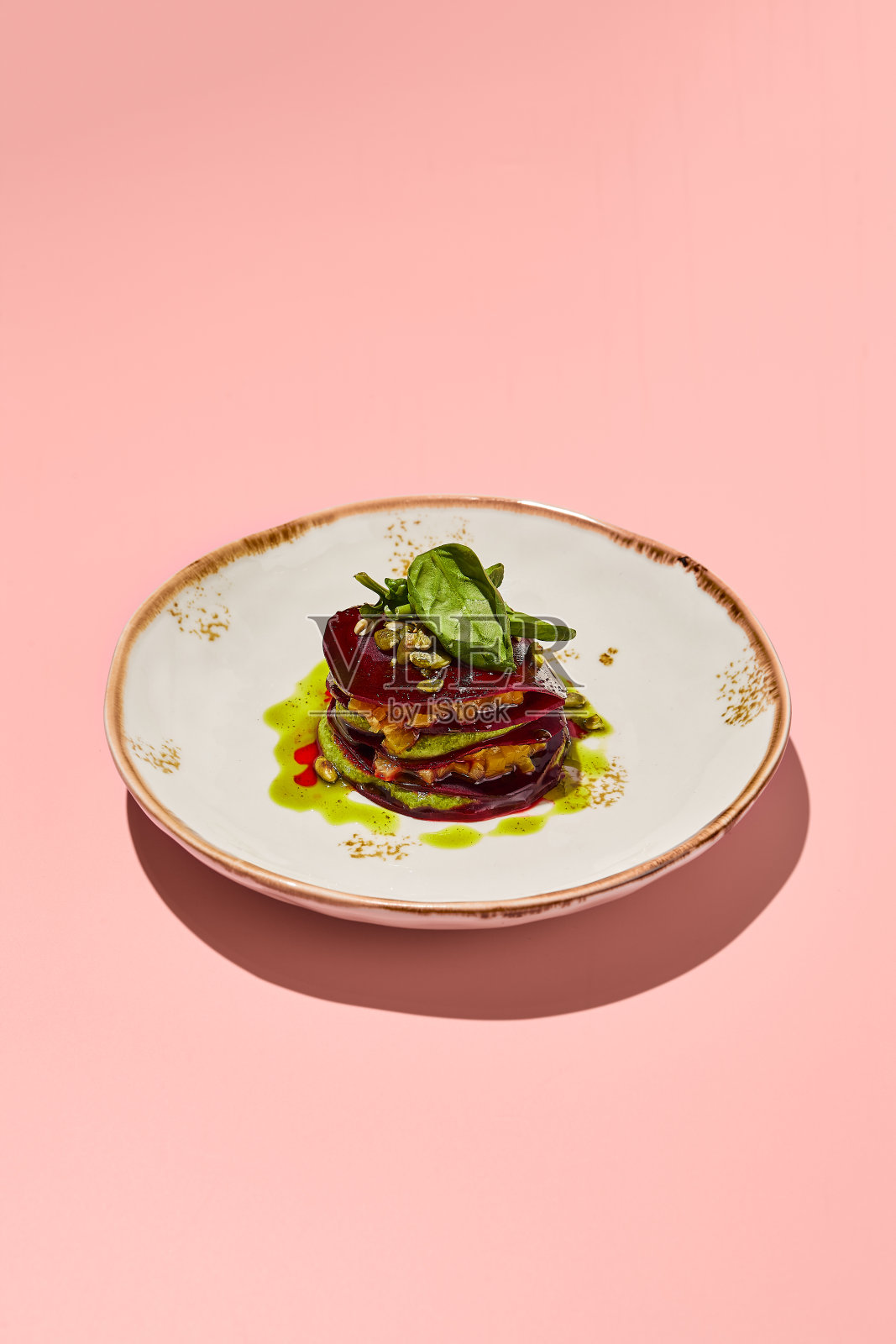 在珊瑚粉色的背景下,一个别致的盘子里放着甜菜根千层香蒜酱,是美食家的素食美食照片摄影图片