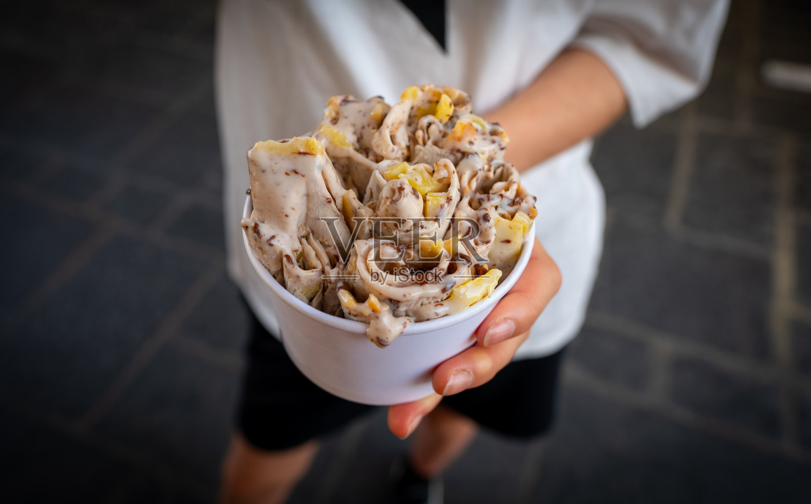 街上女孩手里拿着杯子里的卷冰淇淋。照片摄影图片