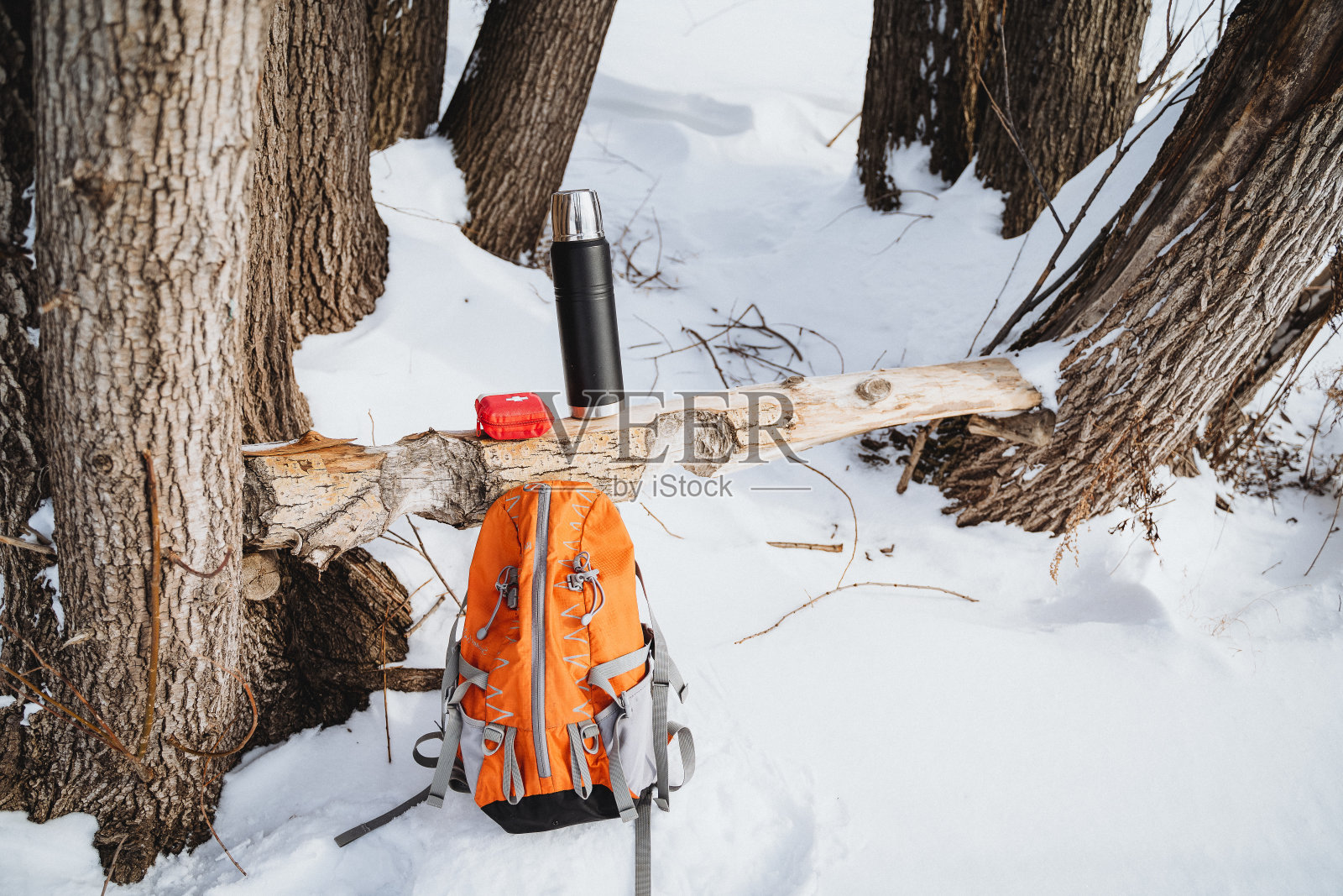 橙色背包,一个保温瓶和一个红色的杯子在雪地森林的背景。照片摄影图片