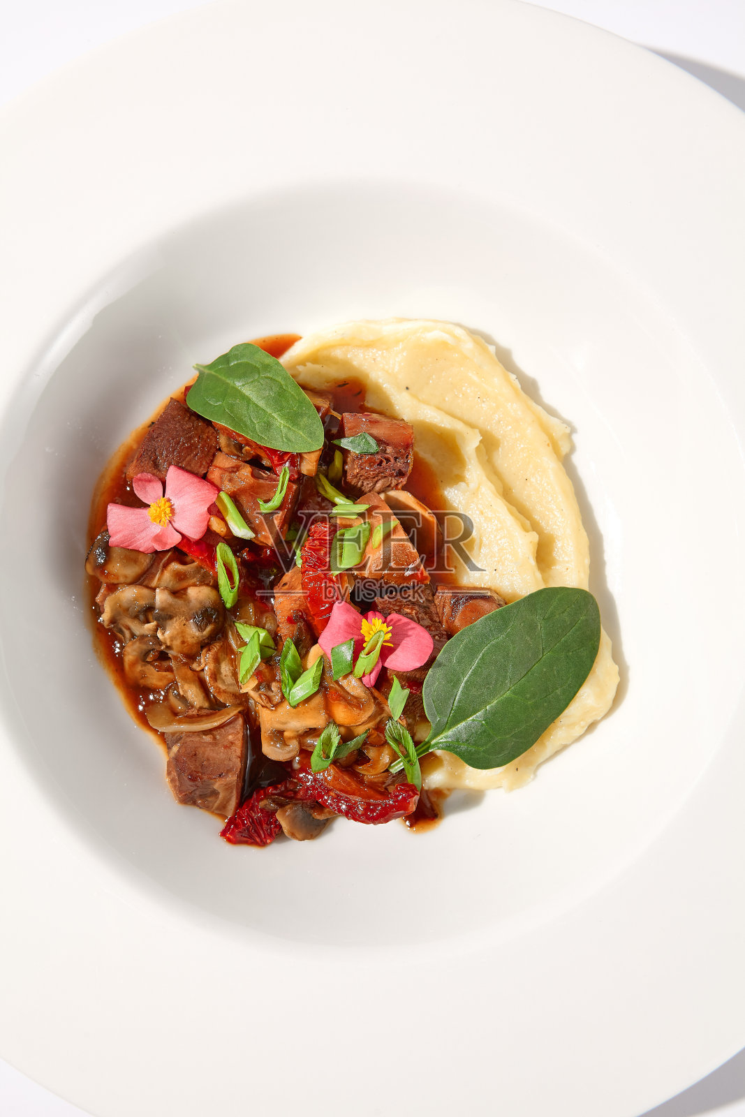 红烧牛肉配蔬菜和蘑菇,顶部是土豆泥,白色背景,俯视图-完美的舒适的食物菜单照片摄影图片