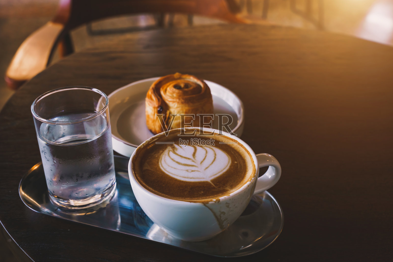 热咖啡拿铁与拉花艺术牛奶泡沫在杯杯和自制葡萄干丹麦白色盘子在木桌子上的顶部视图。在咖啡厅,在咖啡厅,在商务工作期间。照片摄影图片