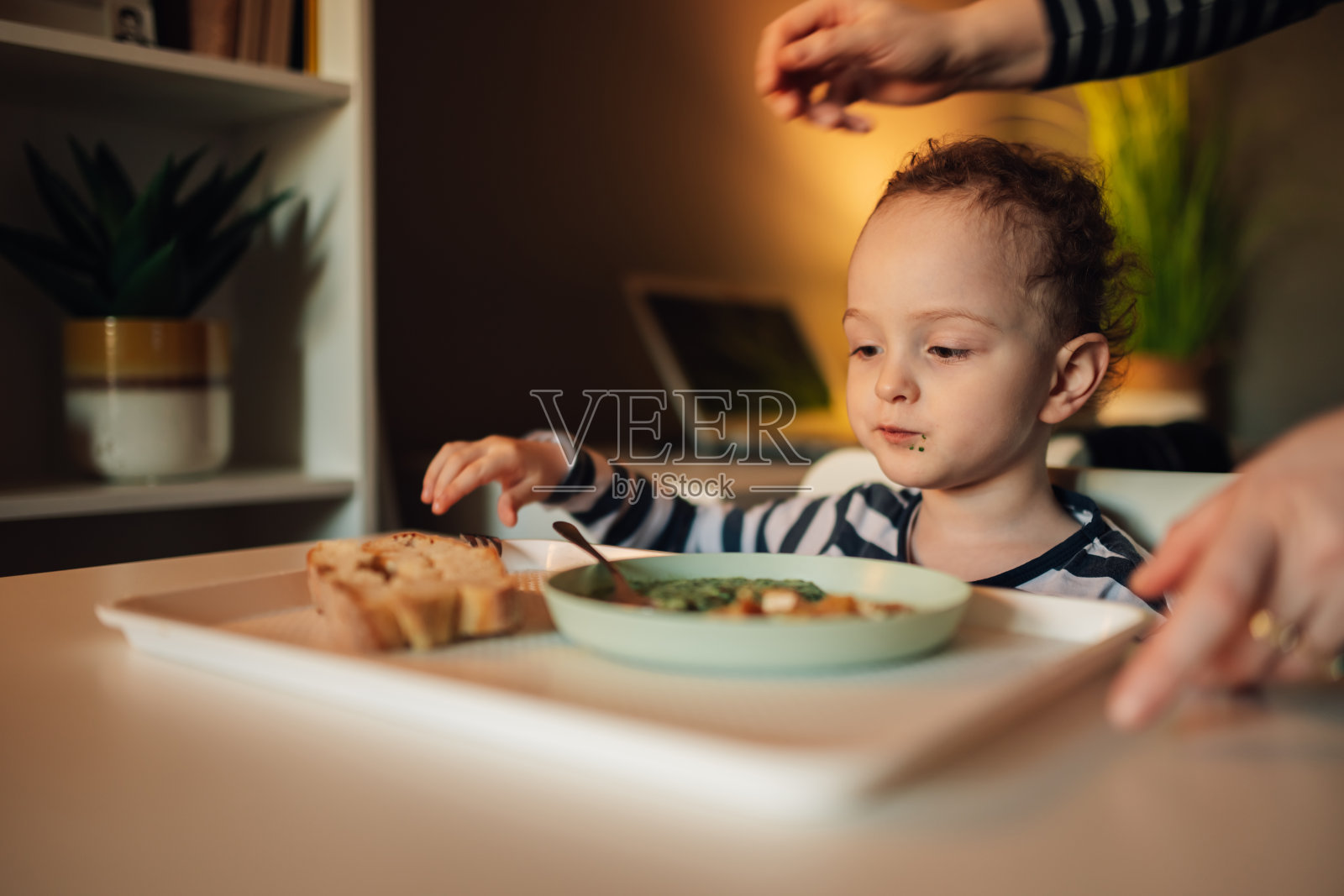 一个饥饿的男孩在妈妈的帮助下正在家里吃东西。照片摄影图片