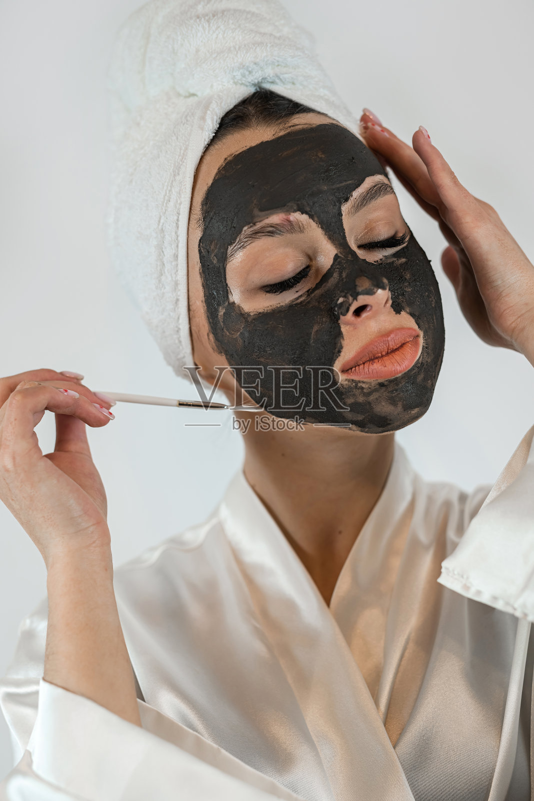 漂亮的年轻女士用刷子把粘土黑色面膜隔离在白色上照片摄影图片