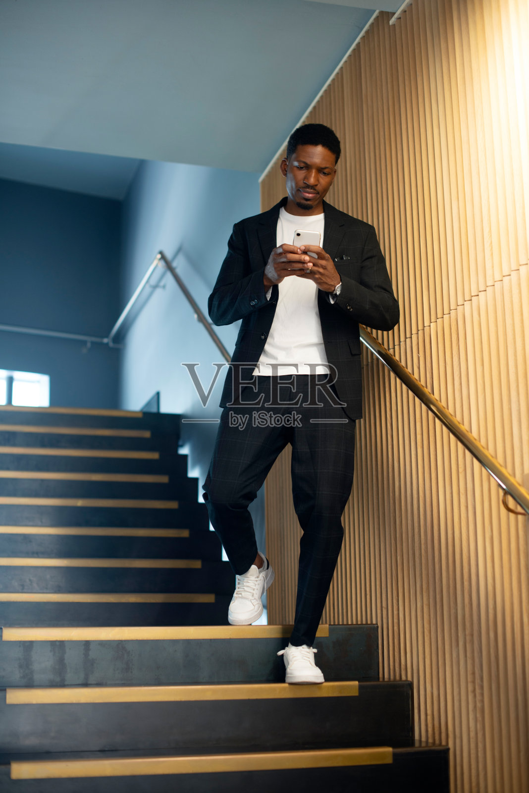 非洲人,在酒店用手机和楼梯发短信、阅读或查看手机应用上的联系通知。人,在纽约用智能手机或走在台阶上,用卷轴写博客、聊天或社交媒体照片摄影图片