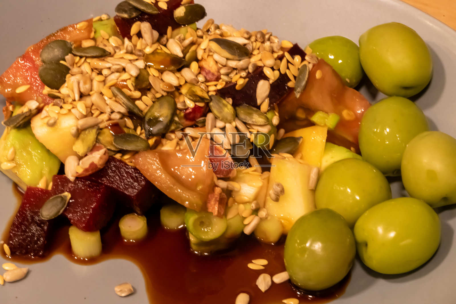 一餐绿橄榄和切碎的沙拉,撒上精选的有营养的种子,并覆盖着香醋,在一个灰色的碗照片摄影图片