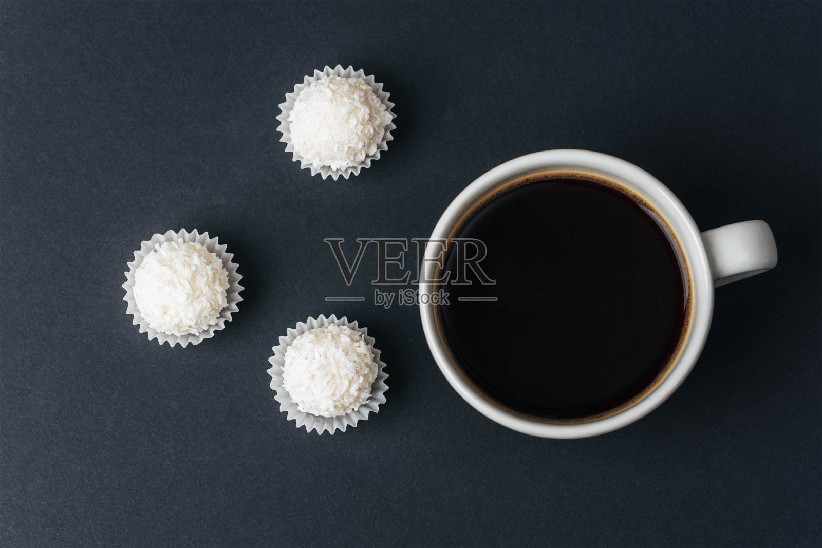 咖啡杯和椰子糖在黑色的桌子上。俯视图,平铺照片摄影图片