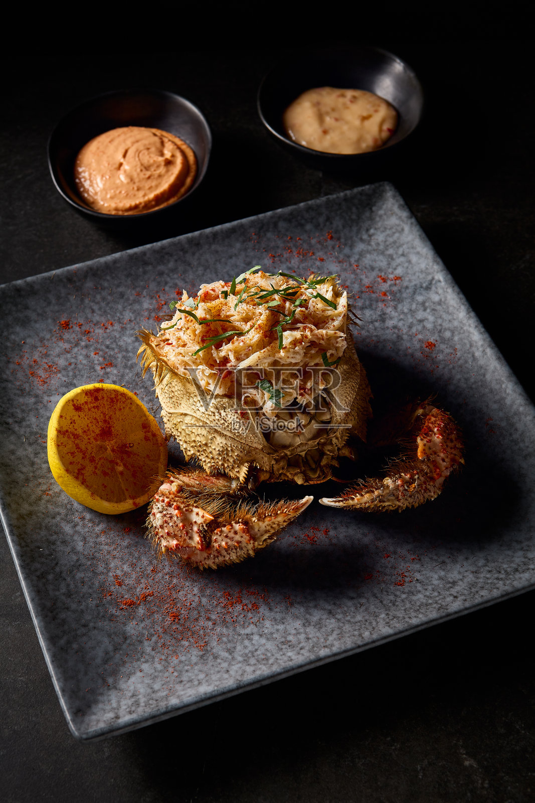 精心清洗过的蟹肉配上柠檬,配上蟹爪和两种酱汁,深色背景搭配低调的摄影风格照片摄影图片