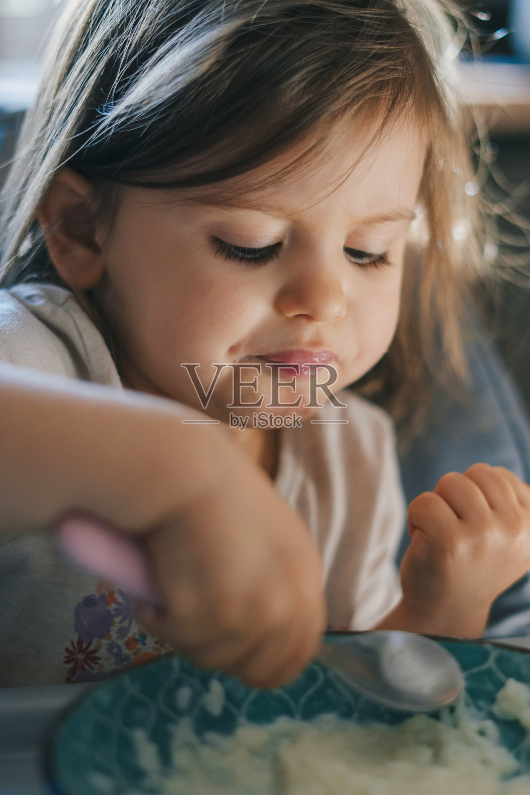 可爱可爱的小女孩坐在高脚椅上用勺子吃粥。孩子的健康饮食。坦诚真实的时刻。照片摄影图片