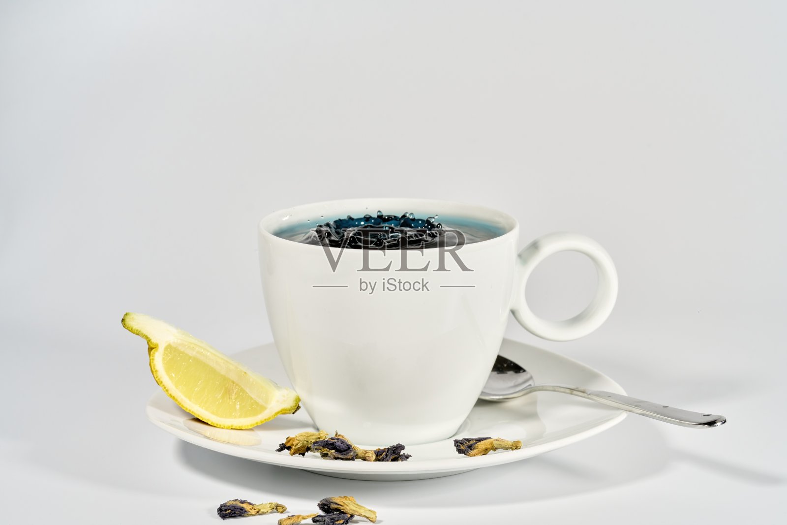 蓝色蝴蝶豌豆茶滴在白色瓷杯与柠檬角照片摄影图片