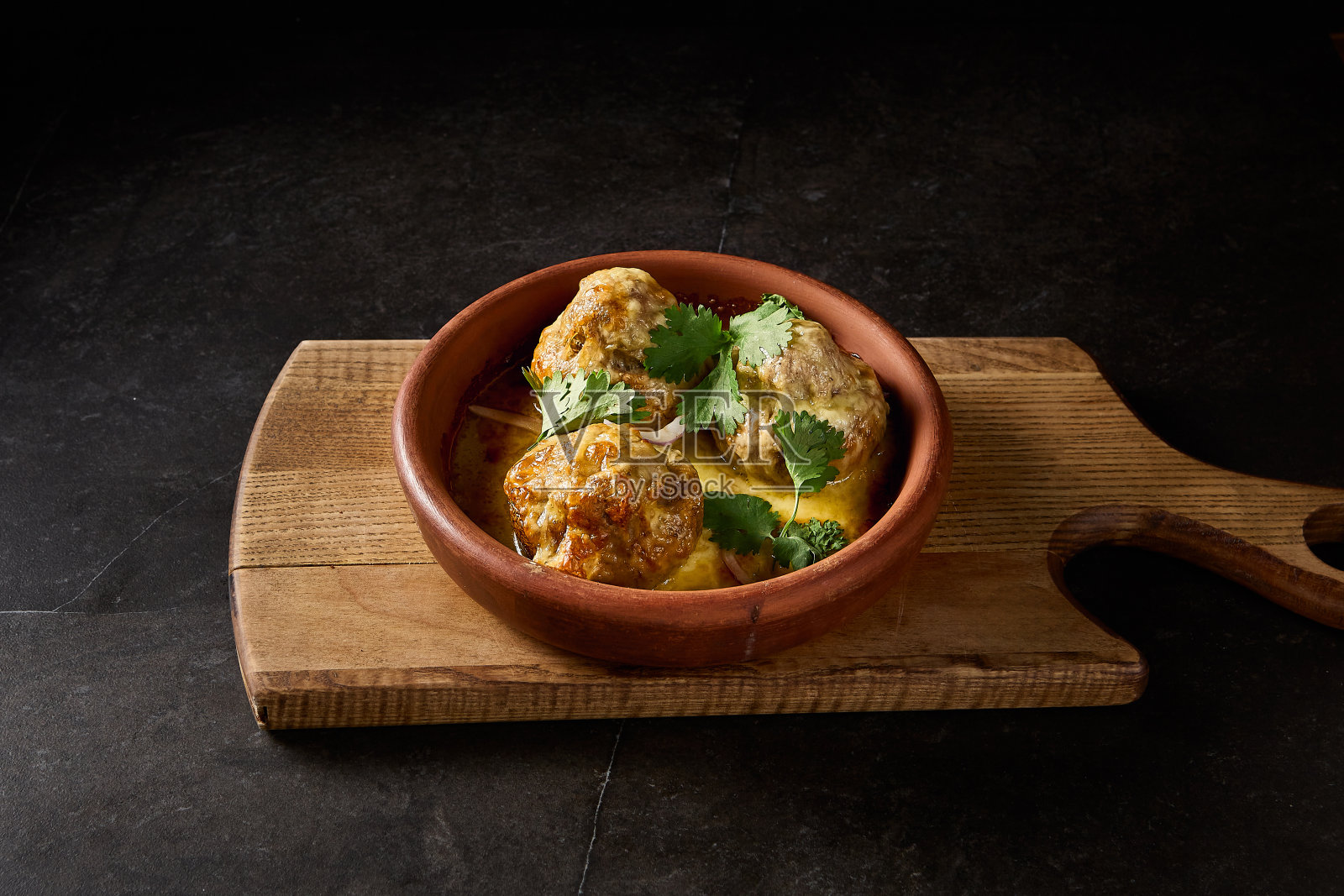 华丽的烤蘑菇的横向视图,大量填充了羊肉和香菜,呈现在格鲁吉亚粘土盘“keci”,在一个黑色的木板上照片摄影图片