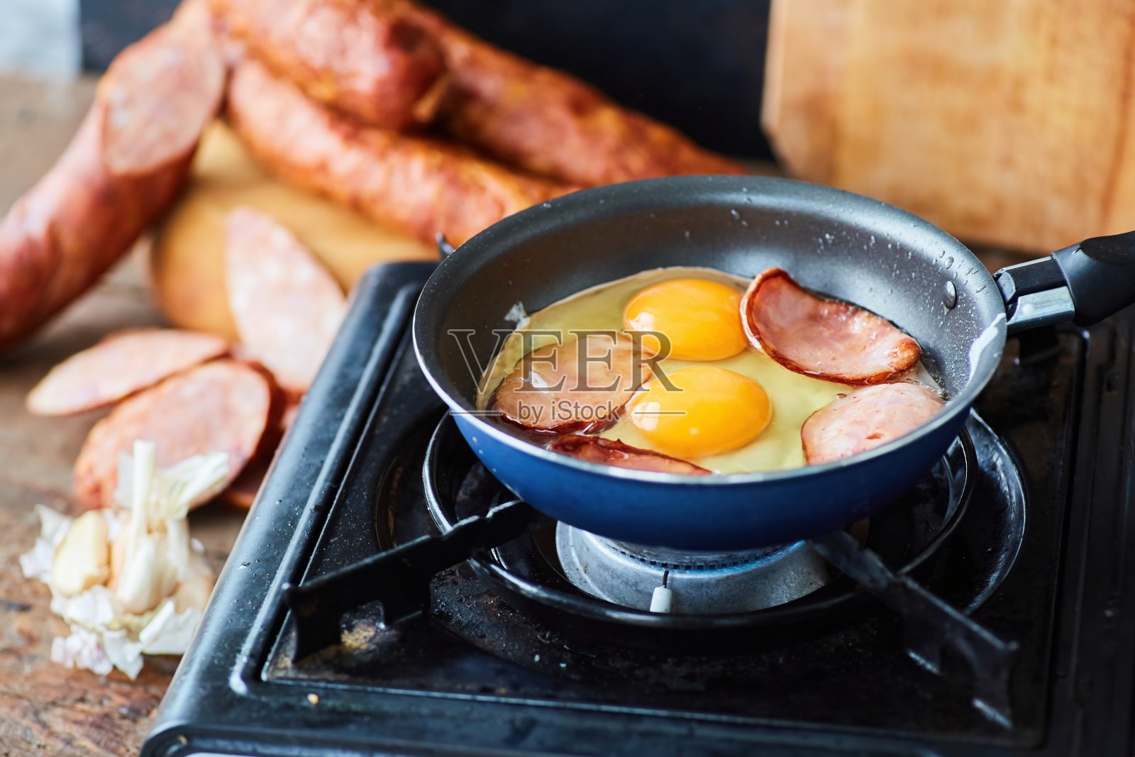 一步一步烹饪这道菜。把香肠和鸡蛋放在平底锅里,放在野营炉上煎。照片摄影图片