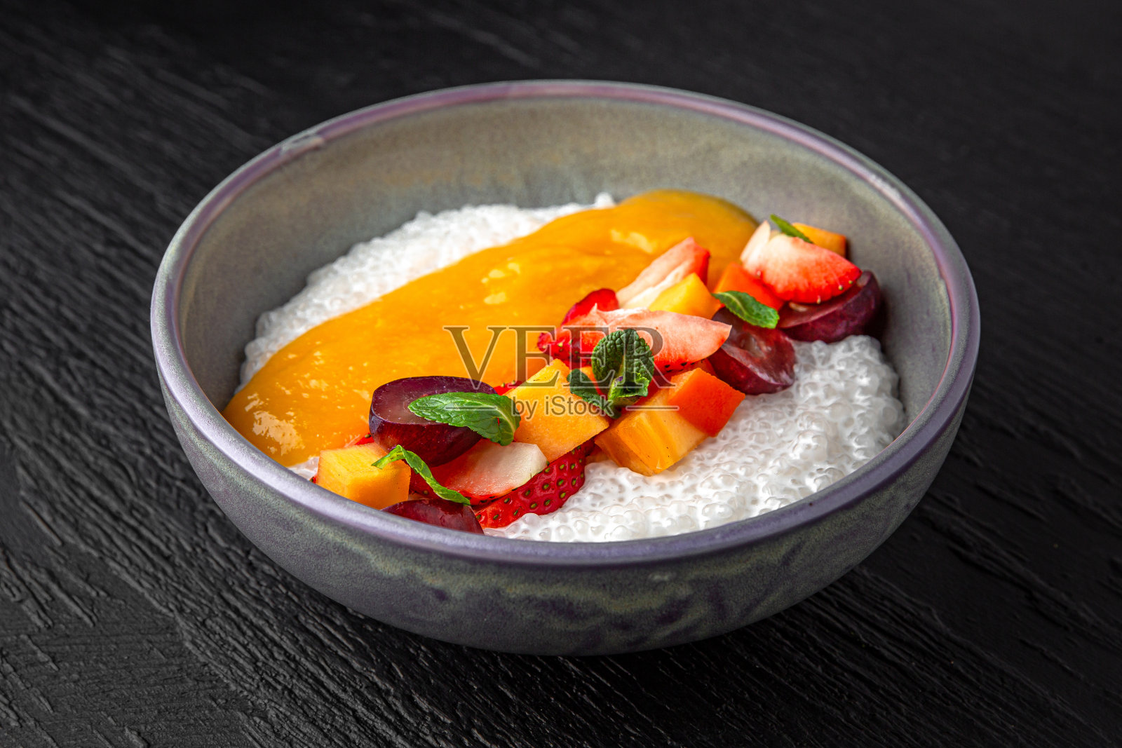 不丰盛的菜单。木薯粥,芒果,桃子泥和浆果在一个陶瓷盘子上深色纹理的背景。餐厅的菜单照片摄影图片