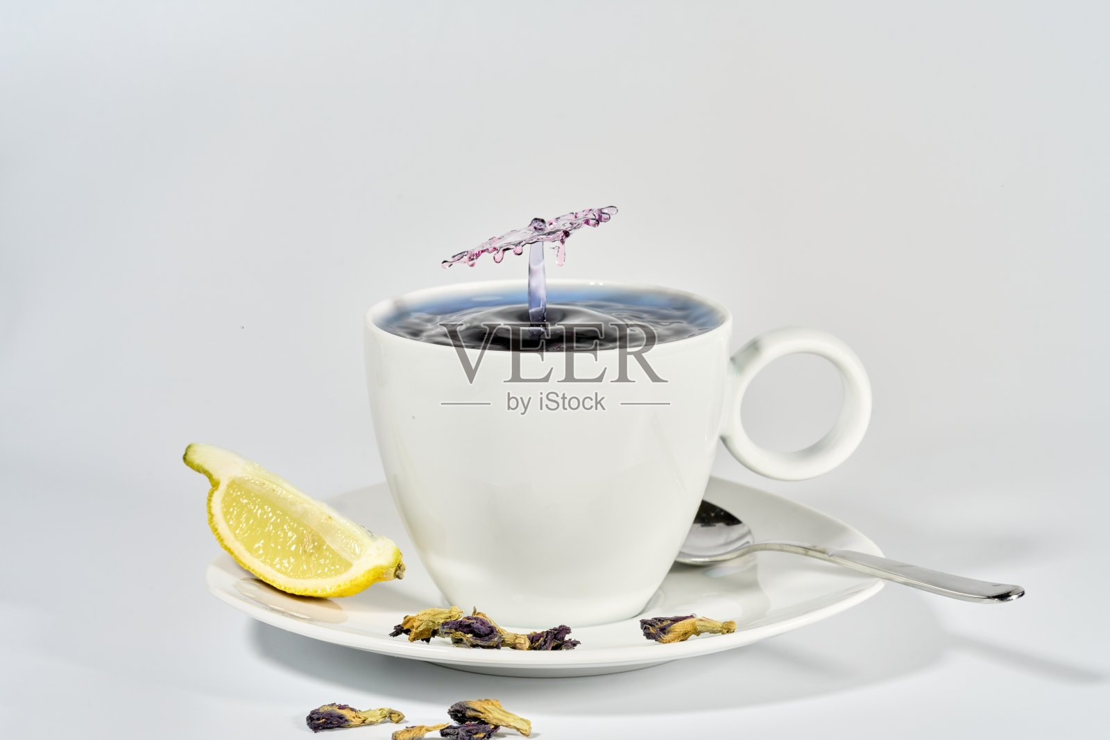 蓝色蝴蝶豌豆茶滴在白色瓷杯与柠檬角照片摄影图片