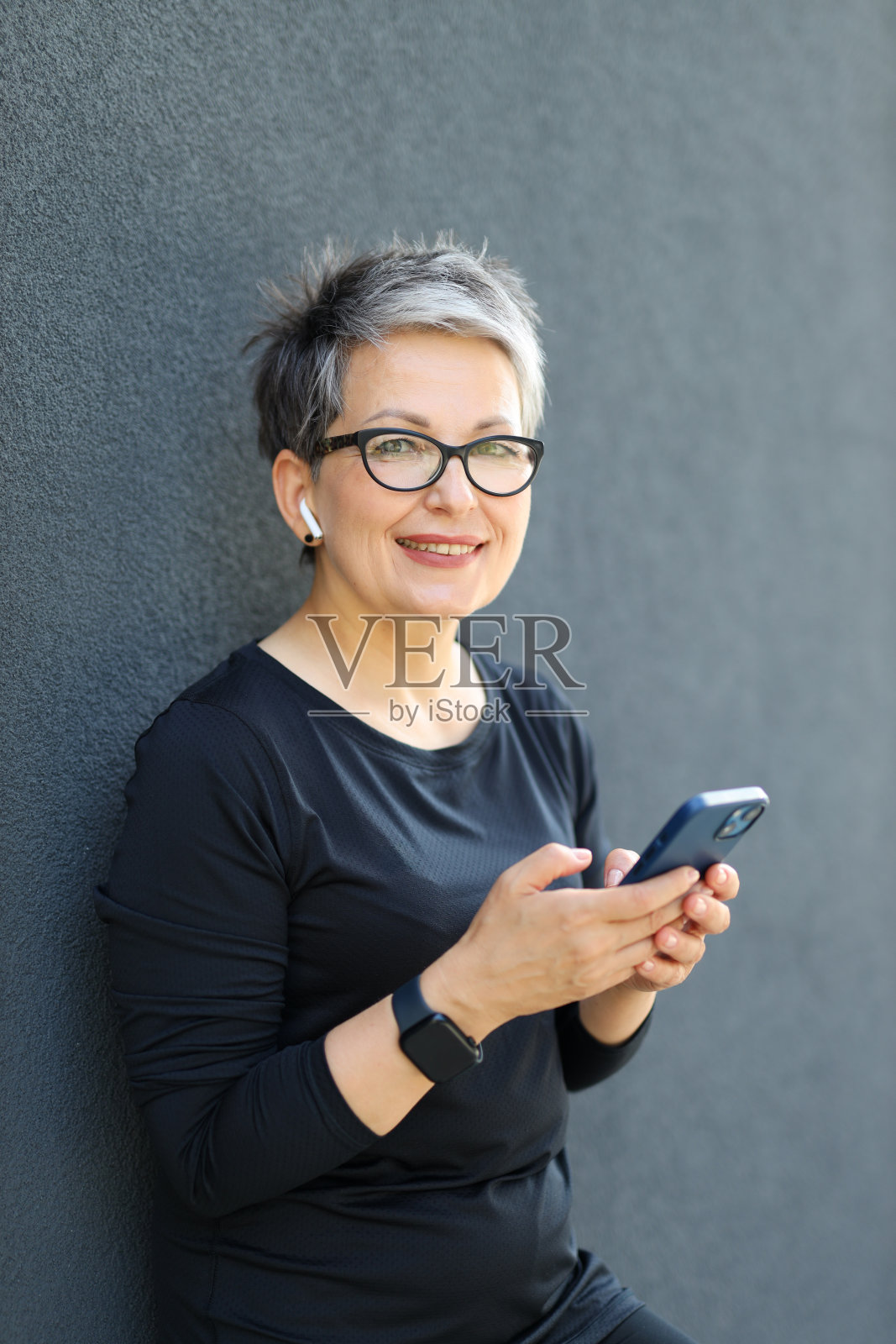 一个成熟的运动女性,一边使用智能手机,一边享受户外休闲,散发着幸福和现代的气息。照片摄影图片