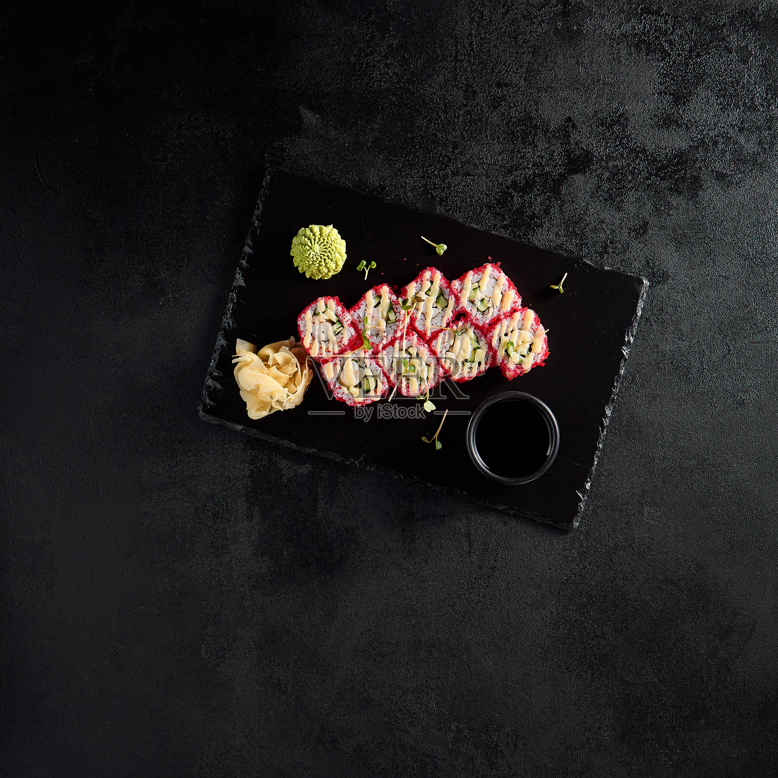 加州卷的俯视图,在黑色石板上放着tobiko和螃蟹,还有酱油、芥末和姜照片摄影图片