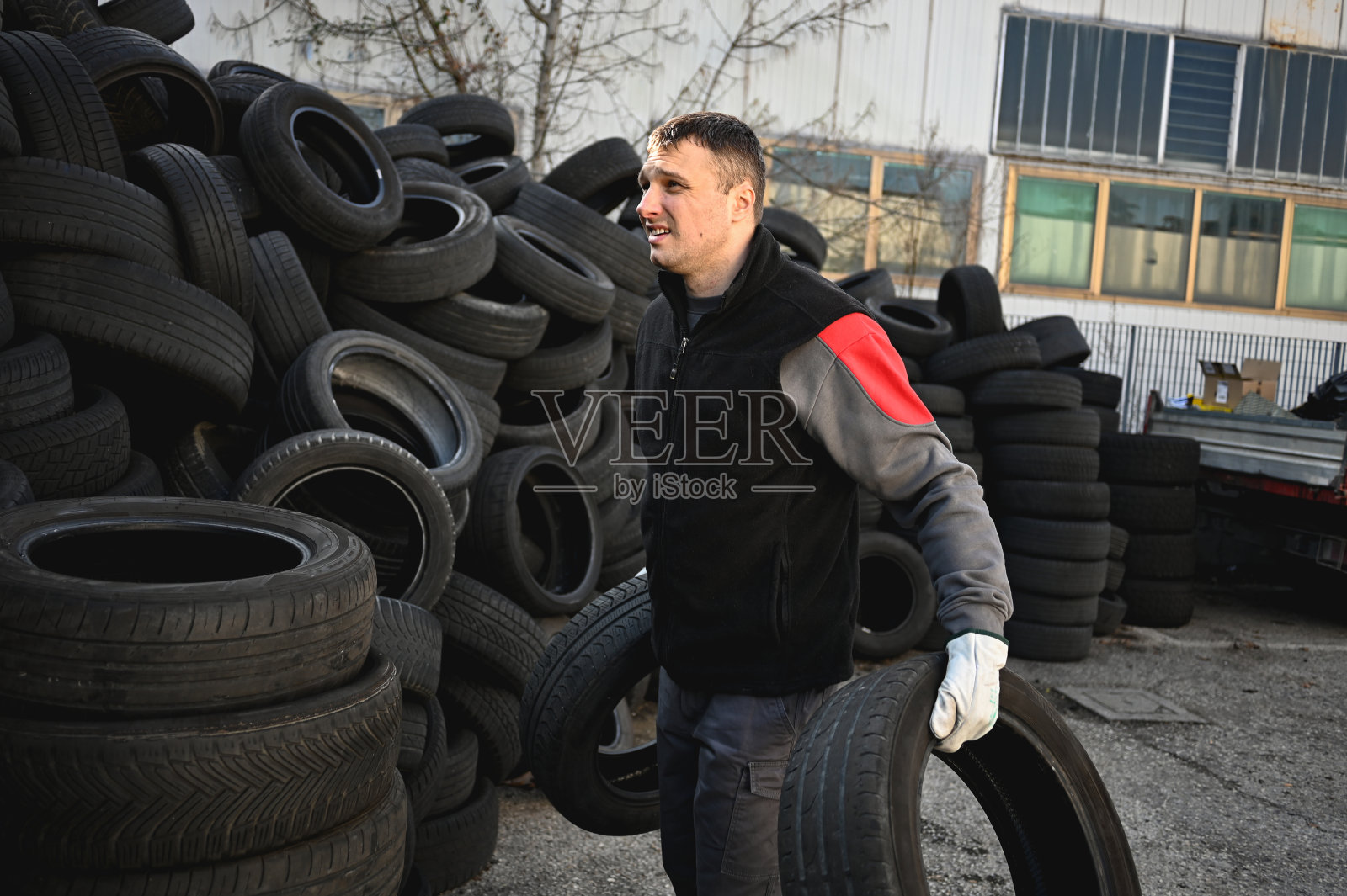 男人扛着堆放的旧轮胎。用旧轮胎填埋。照片摄影图片