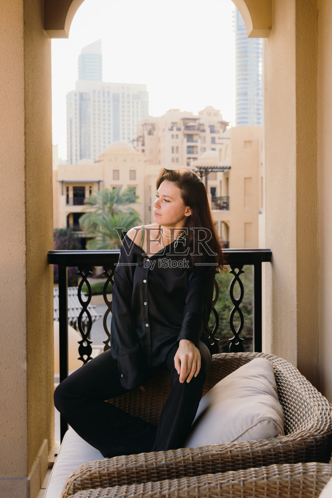 在露台上放松身心,欣赏日落时分迪拜市中心景色的漂亮女人照片摄影图片