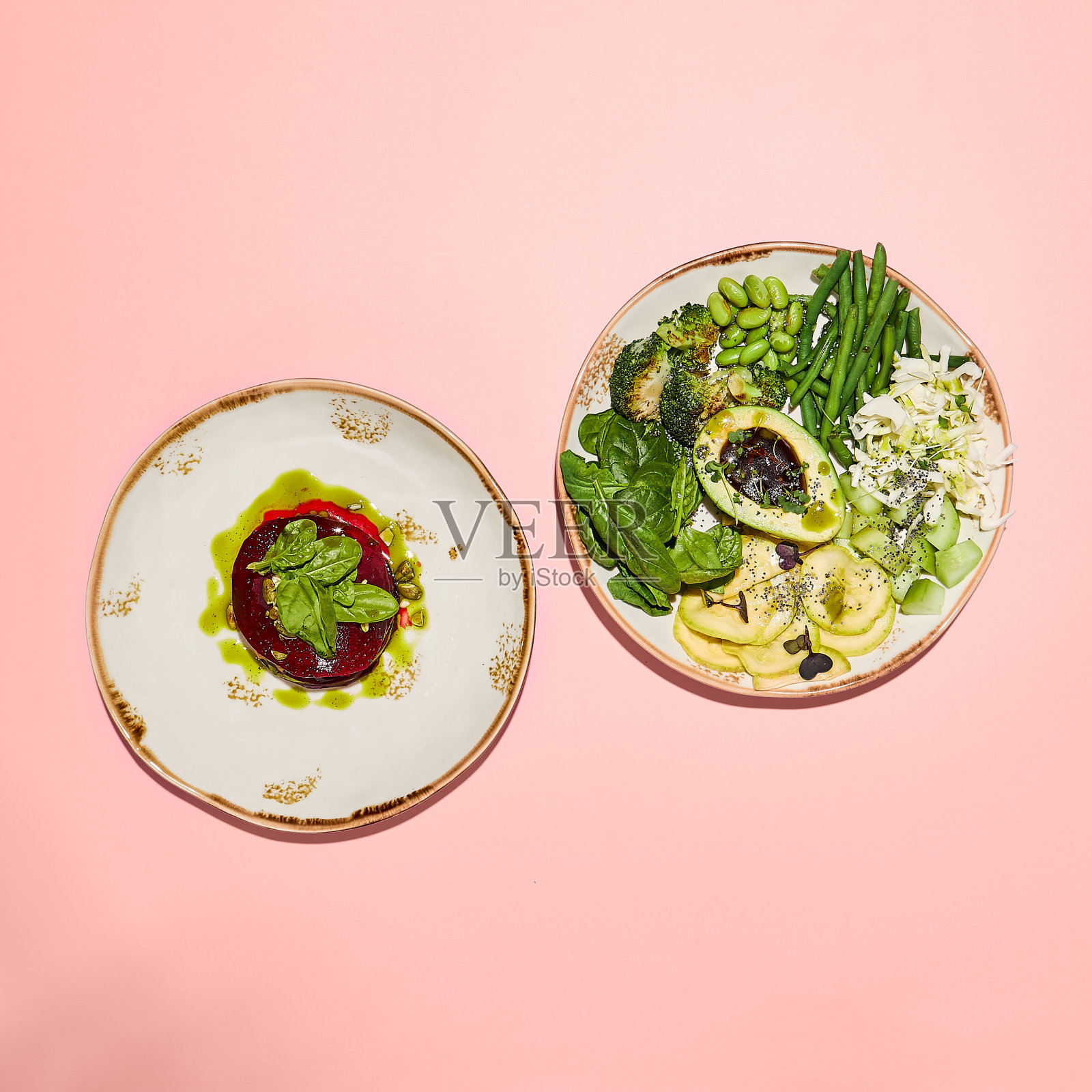 粉色背景上的健康甜菜根千层杂烩和绿色沙拉碗,象征着干净的饮食照片摄影图片