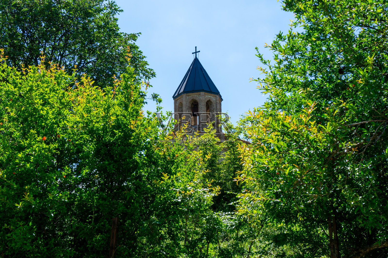 中世纪教堂用石头建造的圆顶和穿过树林的钟楼。天亮,天亮,云绿草绿。格鲁吉亚。照片摄影图片