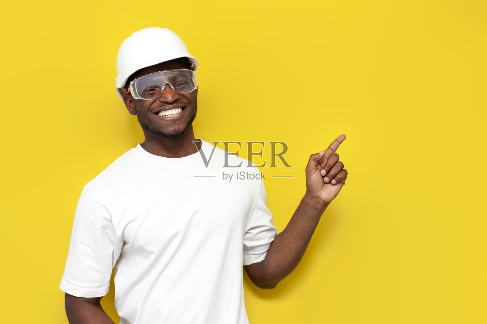 穿着制服的快乐的非裔美国男性建筑工人微笑着向黄色背景的一侧伸出手照片摄影图片