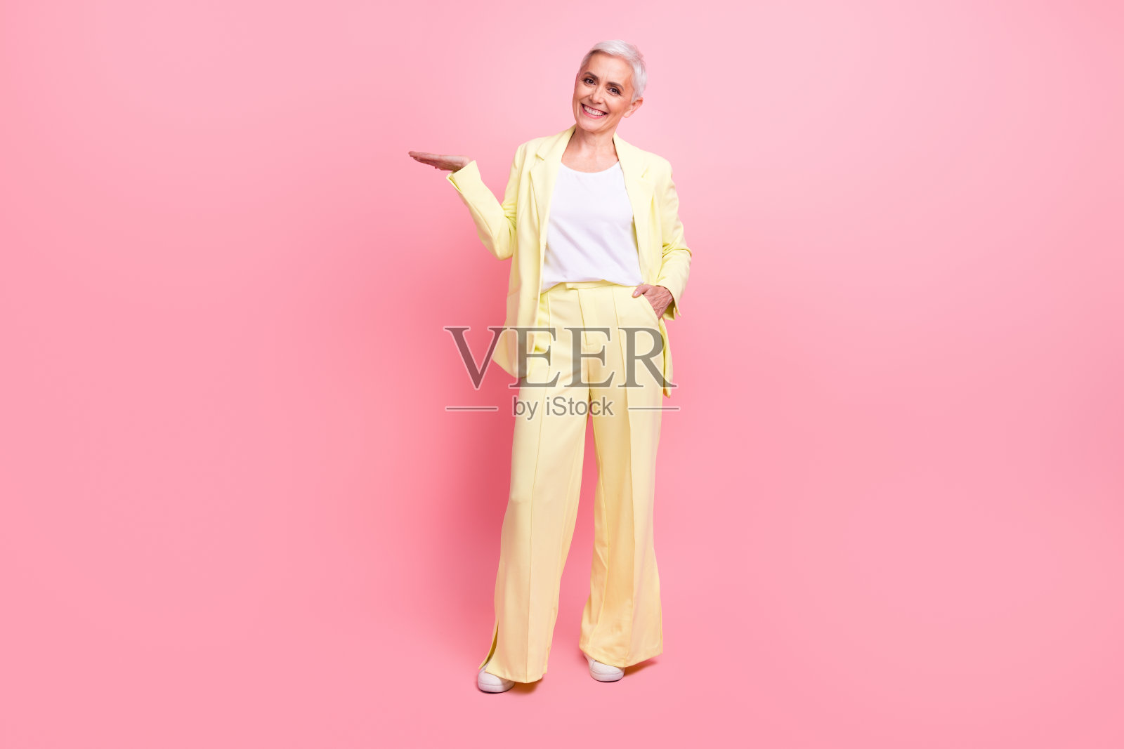 积极开朗的女人穿着黄色西装手掌的全尺寸照片,在粉红色的背景上展示产品的空白空间照片摄影图片