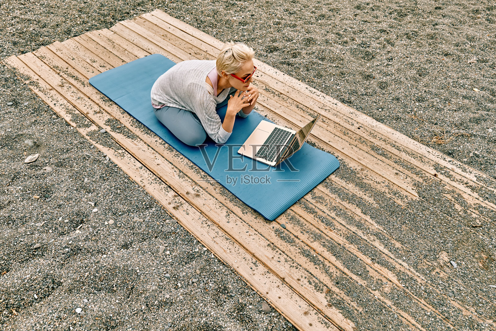 穿着运动服的金发女人,坐在莲花式,在海滩上使用笔记本电脑。自由职业者,幸福的概念。照片摄影图片