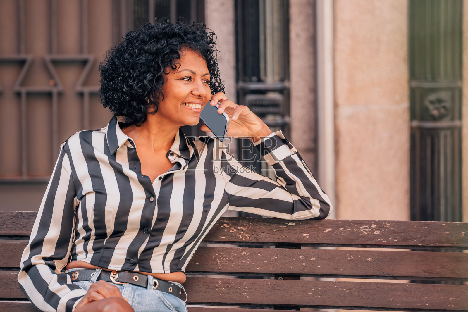 快乐的女人坐在街边的长椅上用手机聊天照片摄影图片