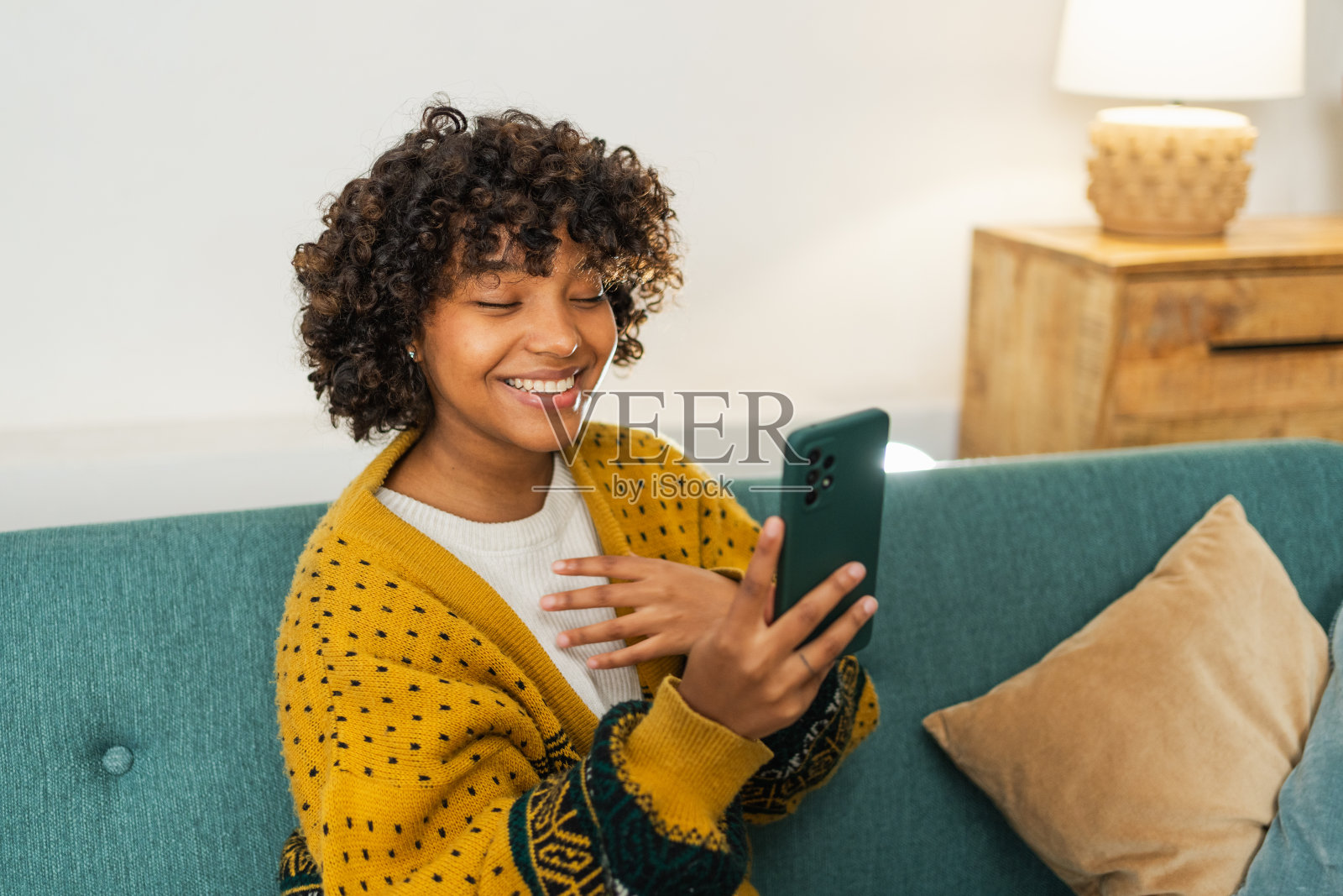 非裔美国女孩拿着智能手机视频聊天。女博主在社交网络上与最好的朋友聊天。年轻女子在家里进行虚拟会议在线聊天视频通话。照片摄影图片