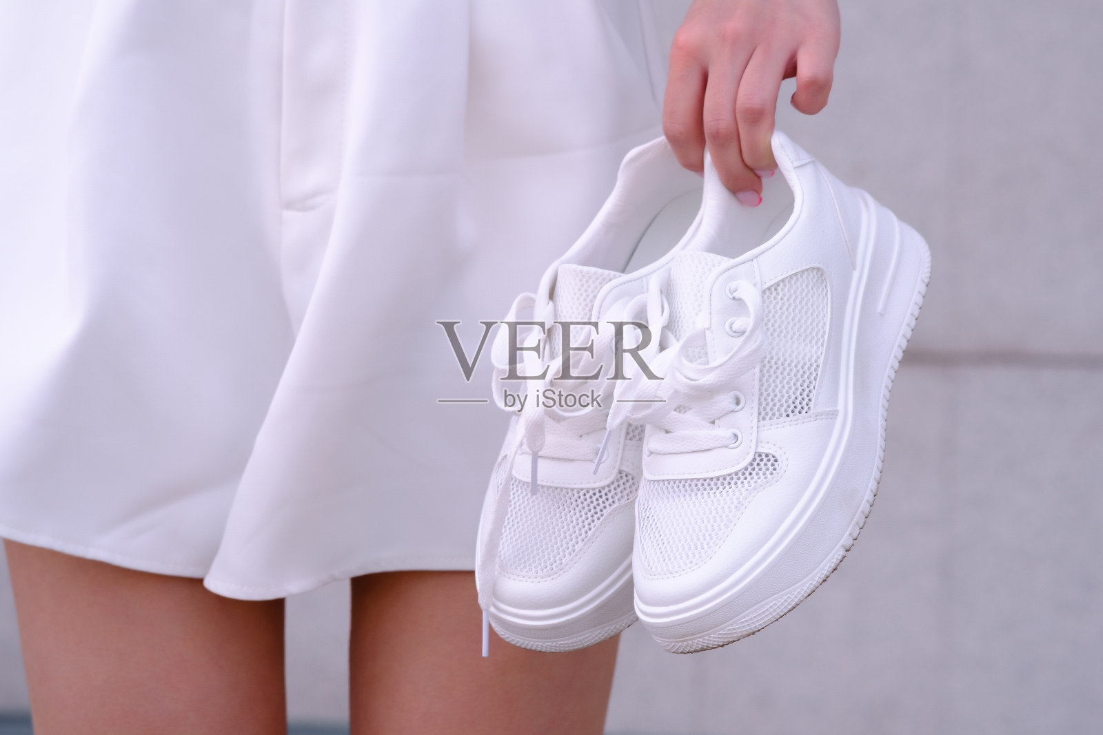一个穿着白色短裤的女孩站着,手里拿着白色运动鞋的特写照片摄影图片