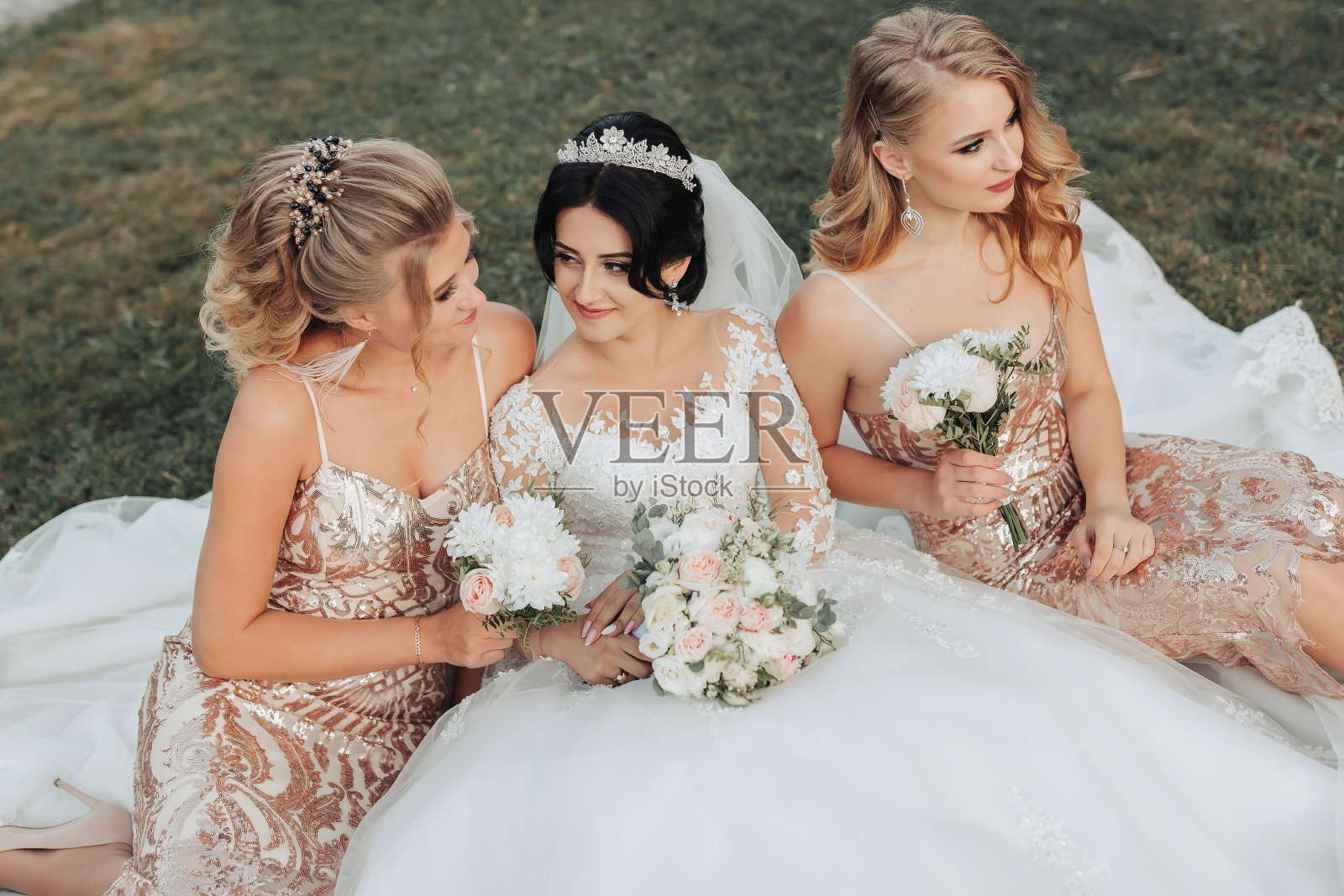 一头黑发的新娘穿着优雅的白色礼服,头戴皇冠,她的金发朋友们穿着金色的礼服照片摄影图片