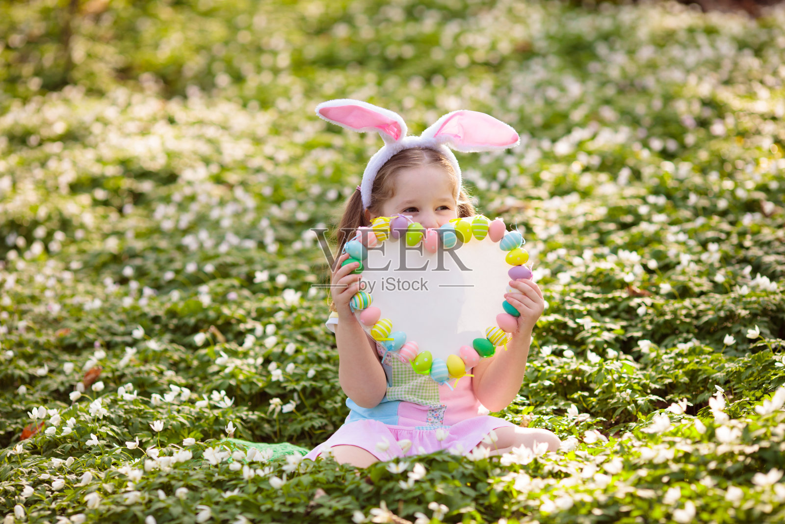 戴着兔子耳朵的孩子在花园里寻找复活节彩蛋照片摄影图片
