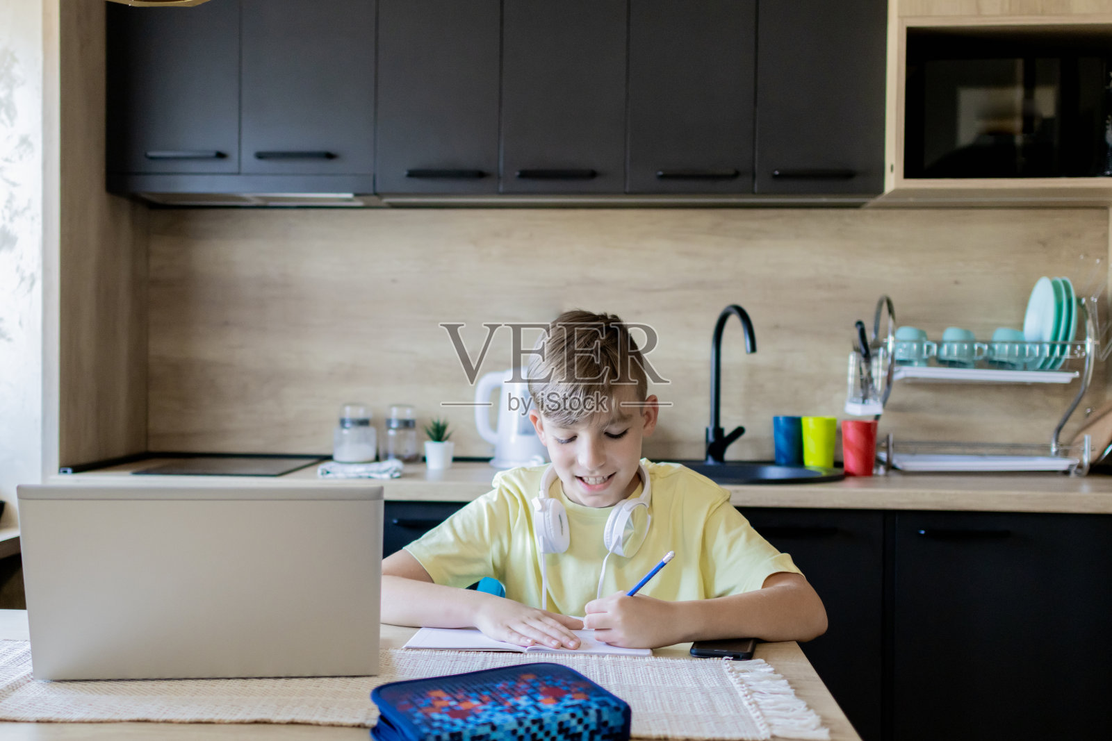 一个男生正在厨房的餐桌上做作业。照片摄影图片