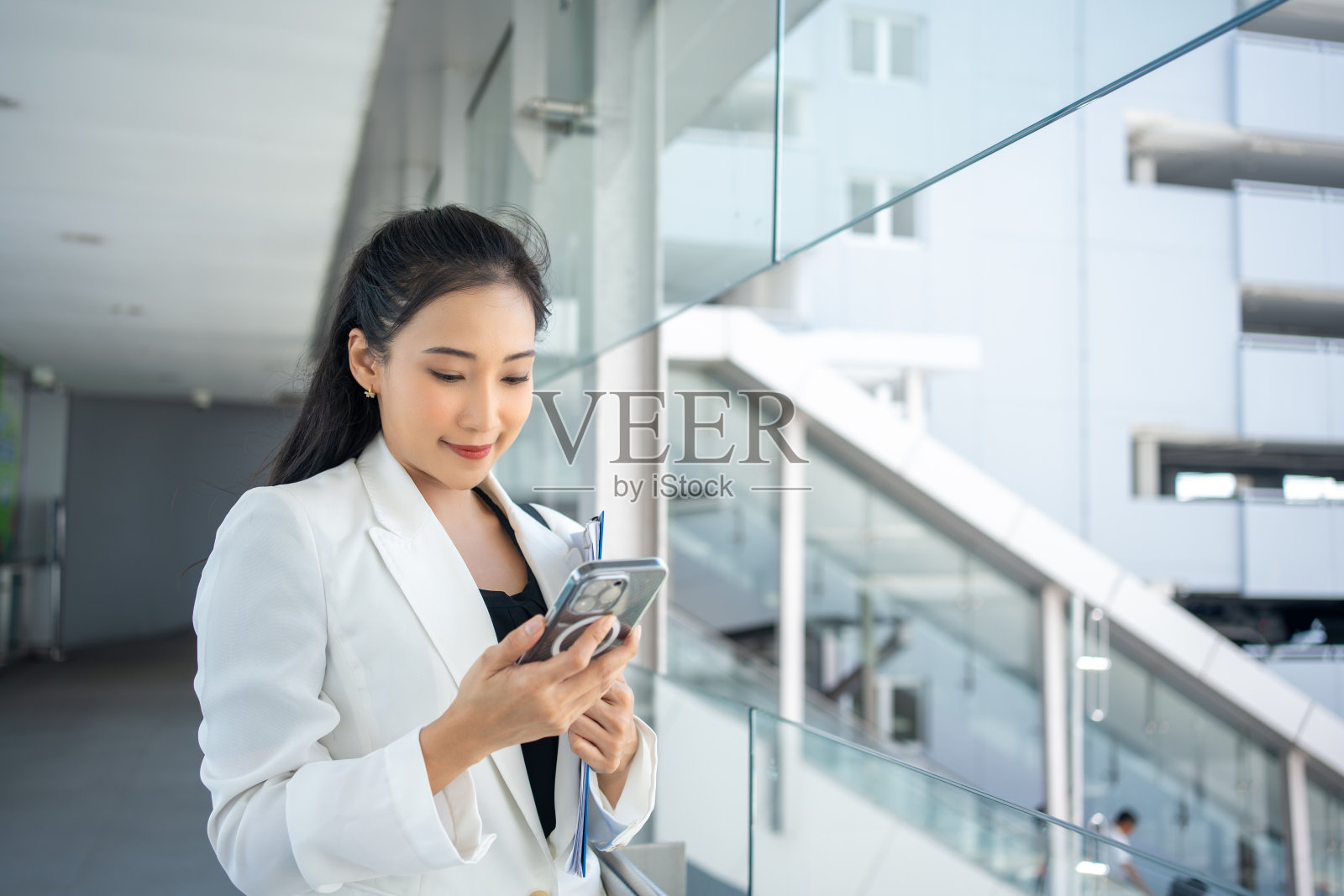 年轻的女商人手持文件,使用智能手机在城市中穿行照片摄影图片