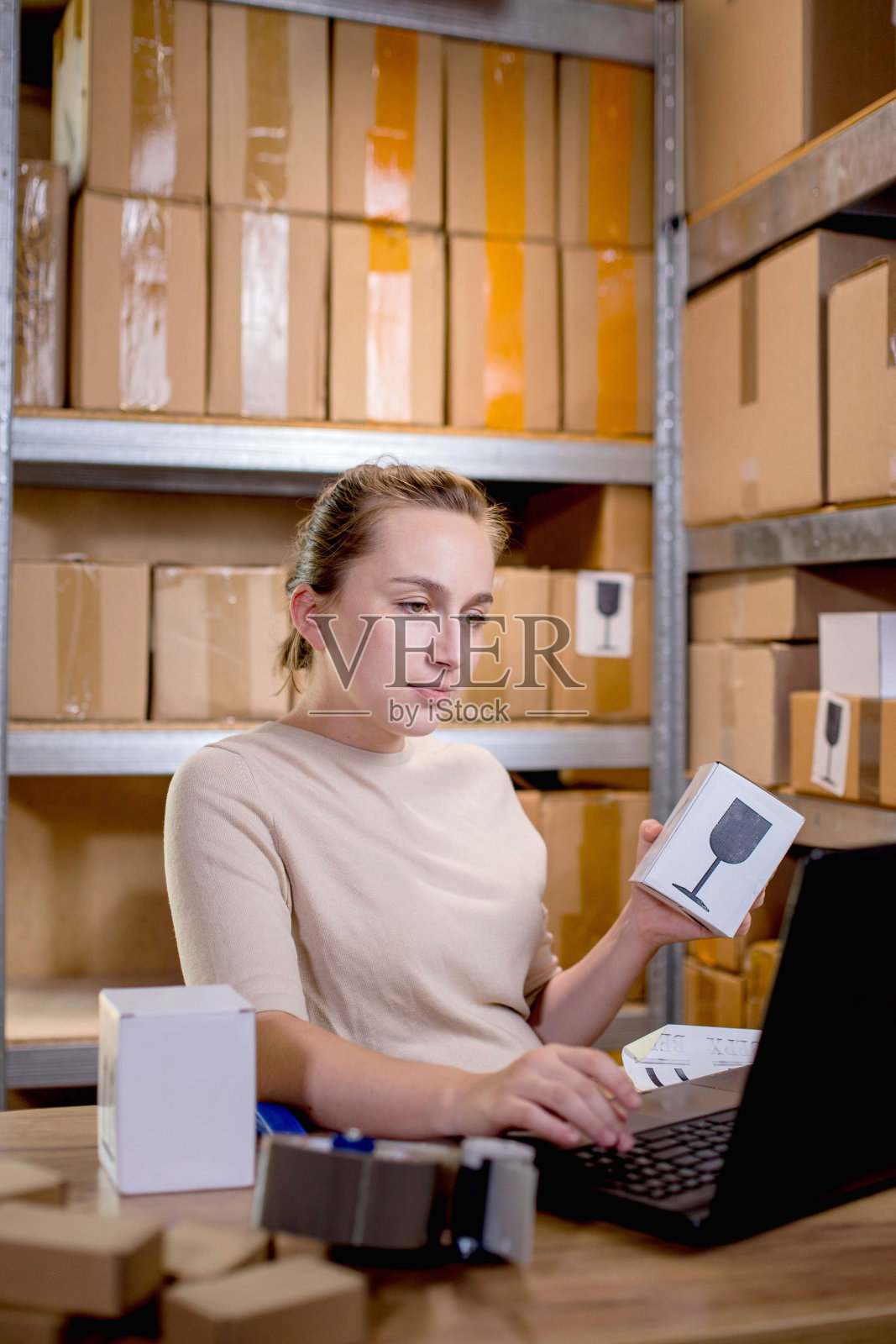 一个女商人拿着盒子,一边准备包裹信息,一边在键盘上敲着什么。邮政服务和小企业的理念照片摄影图片