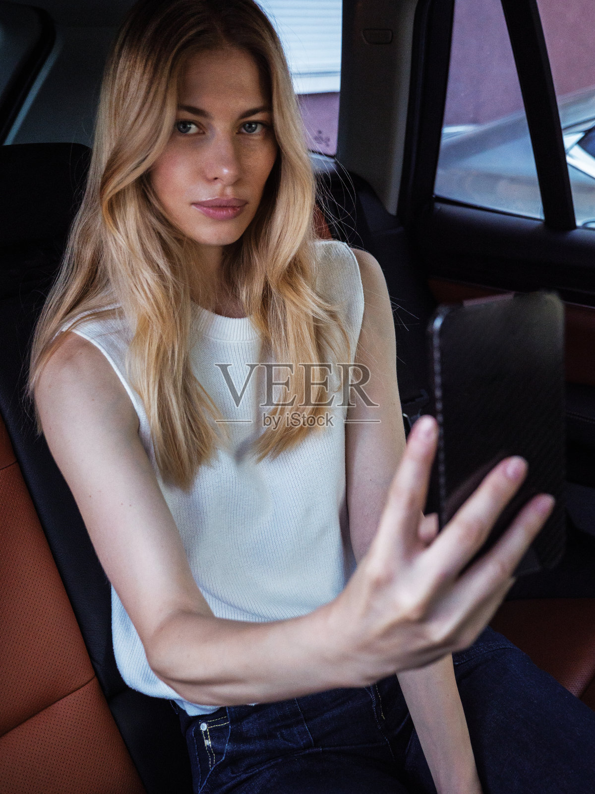 一个年轻的金发女孩喜欢坐在车里和朋友打电话。照片摄影图片