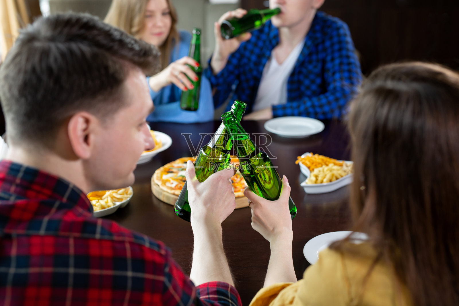 一群年轻的朋友拿着披萨和啤酒在咖啡馆里庆祝照片摄影图片