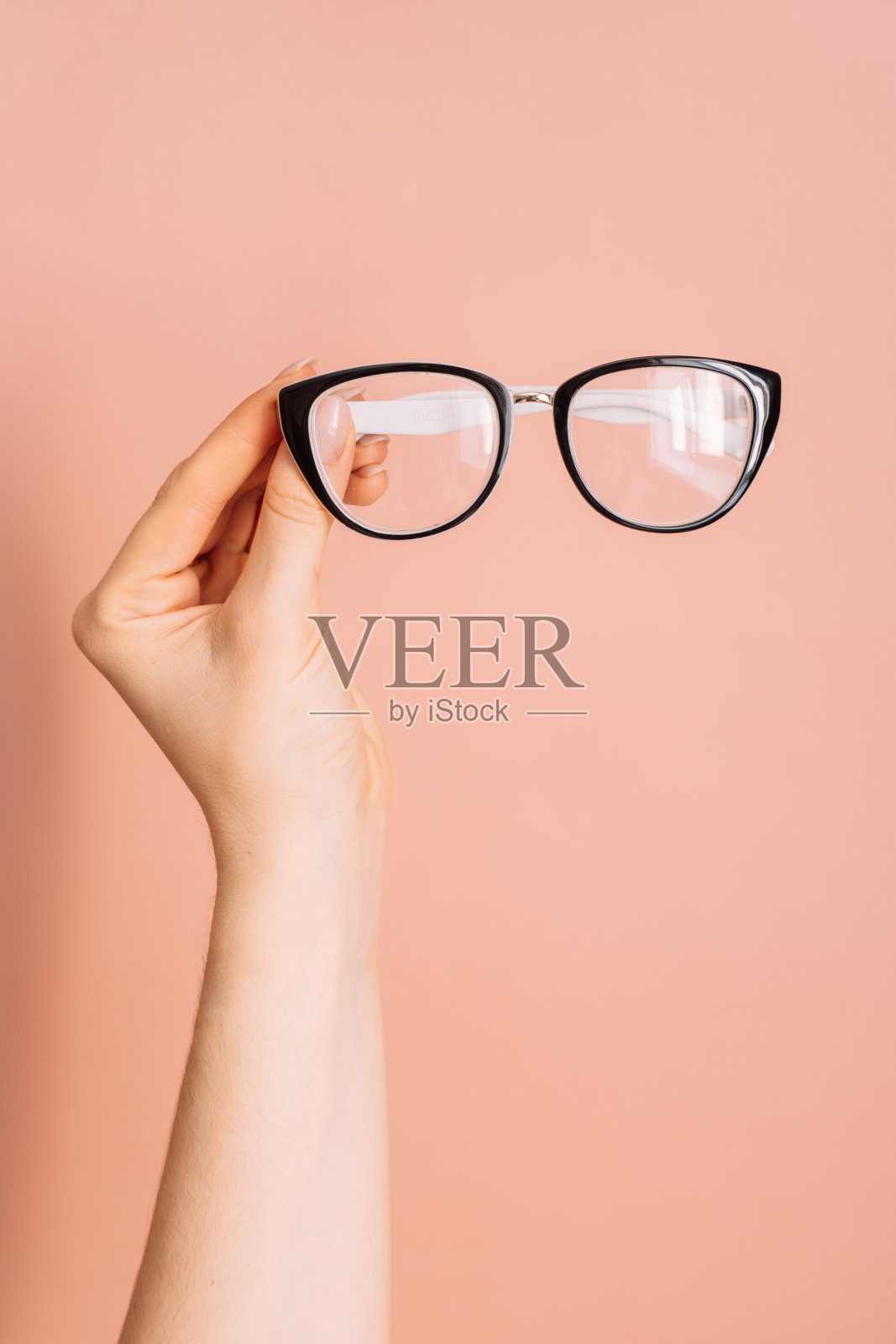 一个女人手里拿着黑色镜框的视觉眼镜,背景是粉红色的照片摄影图片