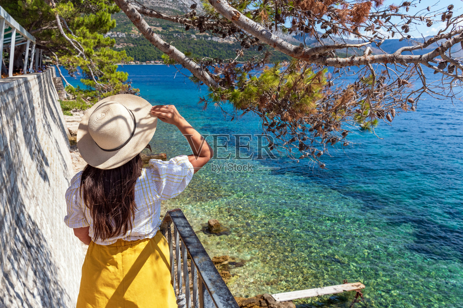 时尚女人站在通往海滩的楼梯上的后视图,在老科尔库拉镇的城墙下照片摄影图片