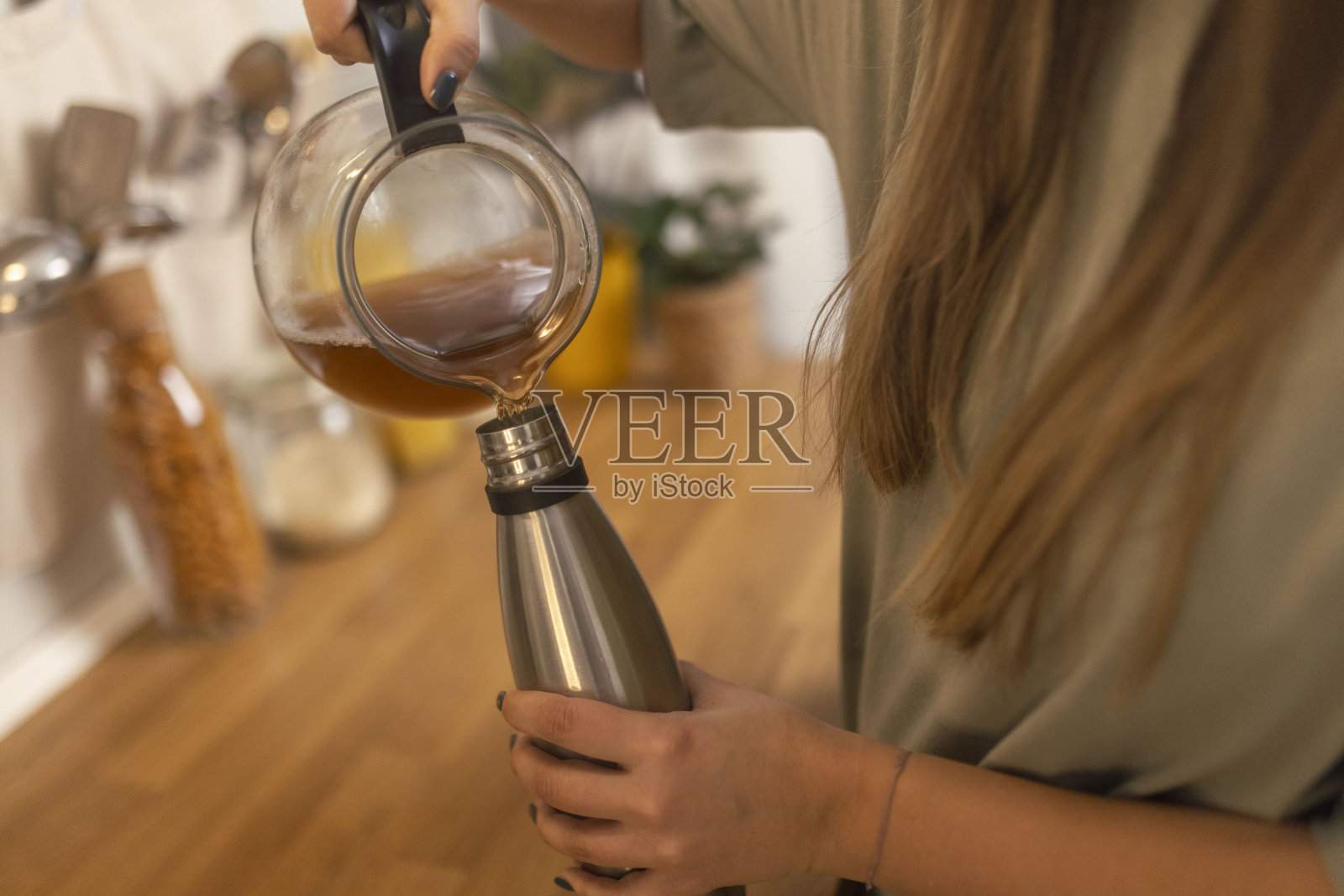 为了保持茶的热度,一个不知名的女人把茶从水壶里倒进一个可重复使用的瓶子里照片摄影图片