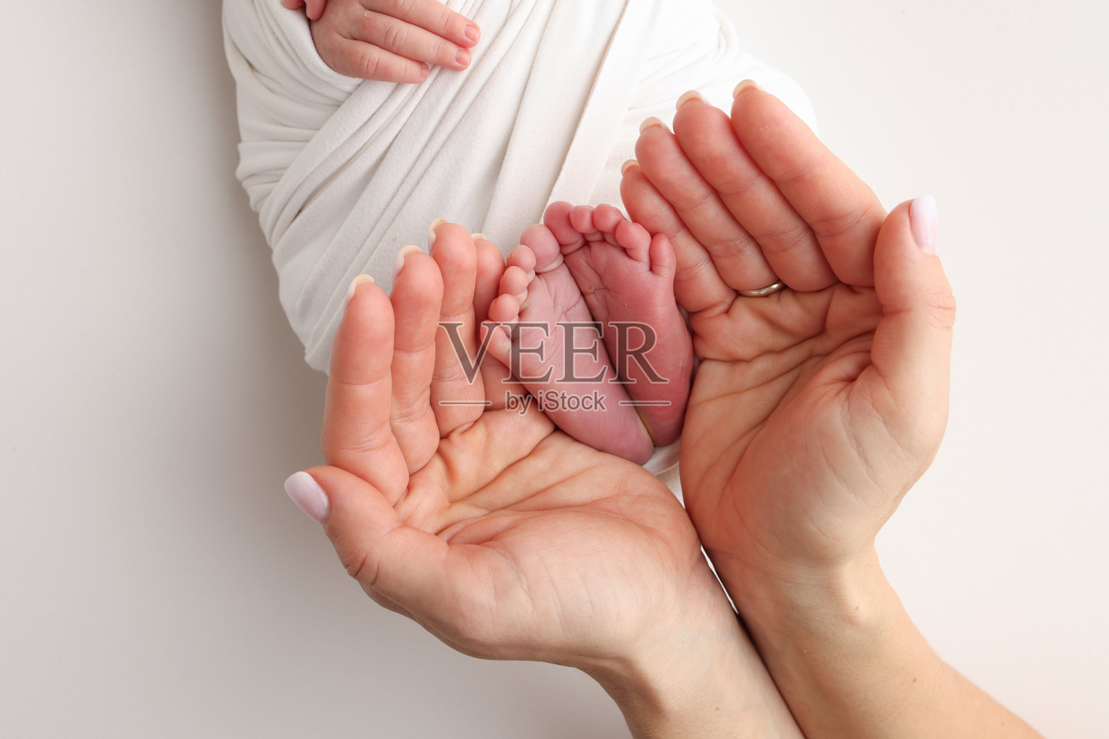 爸爸的手心,妈妈的脚上都抱着刚出生的婴儿的白毯子。新生儿的脚放在父母的手掌上。工作室微距照片的一个孩子的脚趾,脚跟和脚。照片摄影图片