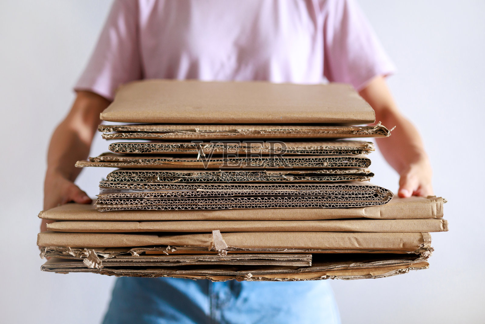 一名亚洲妇女拿着一堆折叠的纸板,准备回收,展示了一种可持续的生活方式照片摄影图片