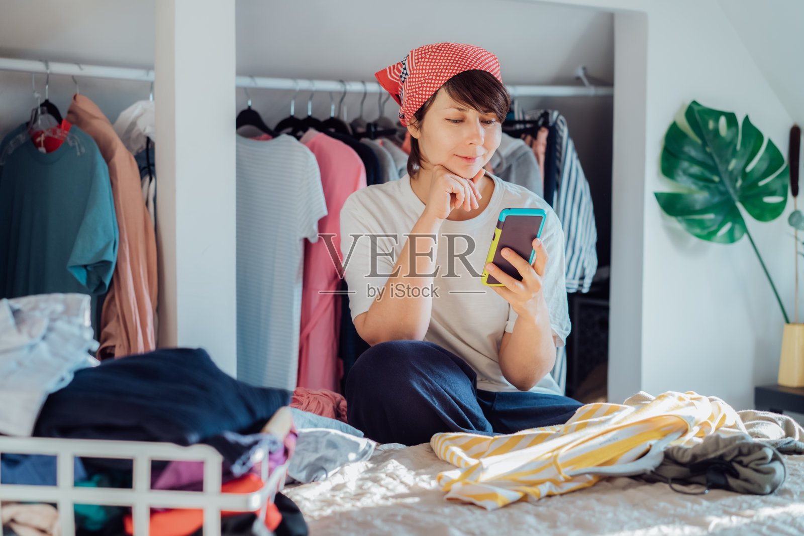 微笑的女人用智能手机寻找捐赠或出售衣服的地方。整理、分类和清理衣物。有意识的消费者,可持续性。再利用,二手,慈善的理念照片摄影图片