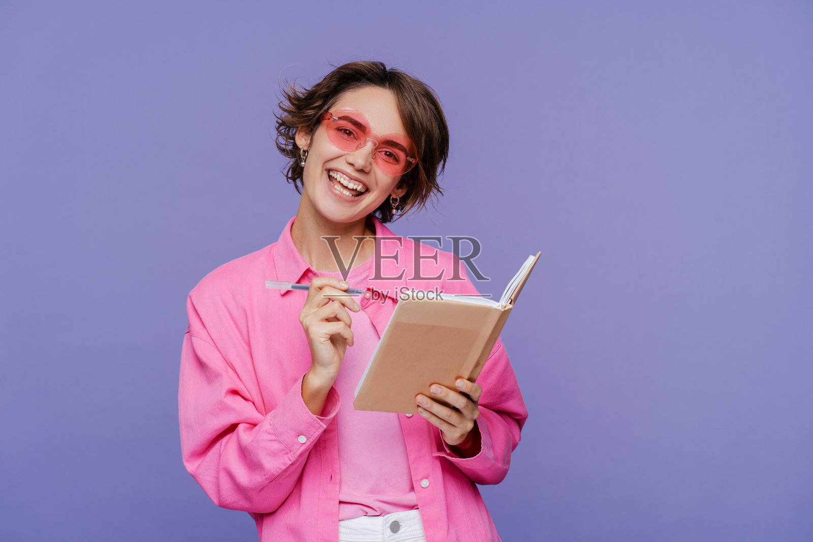 微笑的美丽女学生的肖像拿着书和笔,看着相机照片摄影图片