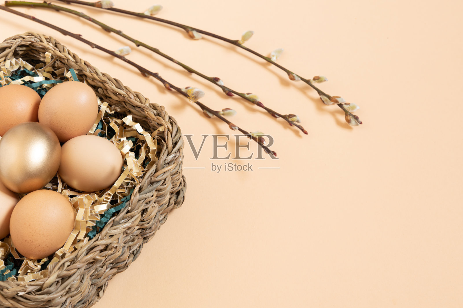 复活节彩蛋自然和黄金在篮子与金色和绿色的纸填料。柳絮枝。淡粉色的橙色背景与复制空间照片摄影图片
