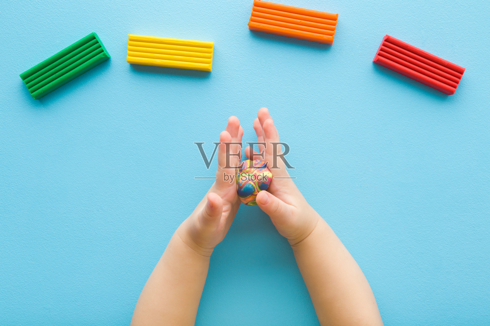 在浅蓝色的桌子背景上,小男孩的手滚动着粘土造型的彩球。柔和的颜色。特写镜头。视角镜头。幼儿的发展。使形状。自顶向下视图。照片摄影图片